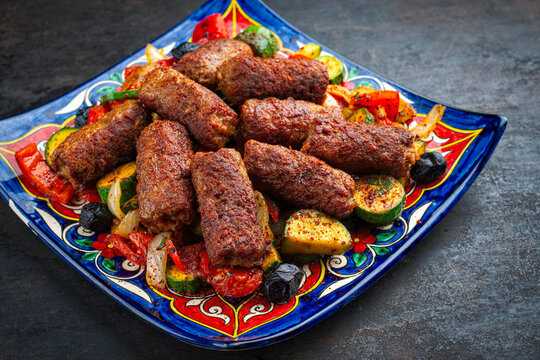 Traditional Croatian cevapi spicy meat ball rolls with troasted vegetables served as close-up on a rustic plate