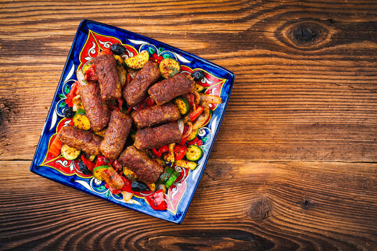 Traditional Croatian cevapi spicy meat ball rolls with troasted vegetables served  as top view on rustic design plate