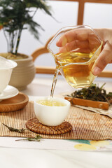 Traditional Tea Ceremony - Pouring Golden Tea from Glass Pitcher into White Cup on Bamboo Mat