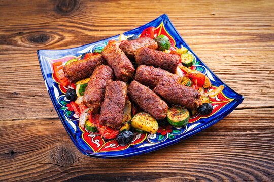 Traditional Croatian cevapi spicy meat ball rolls with troasted vegetables served as close-up on a rustic plate
