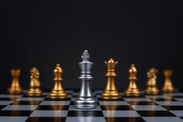 White chess king surrounded by black pieces on chess board