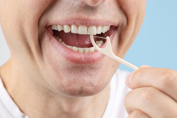 Man brushing teeth with toothpick with dental floss on blue background