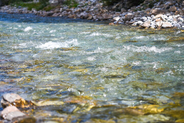 Clear alpine stream with flowing water and visible stones on the riverbed in the Glarus Alps, Switzerland