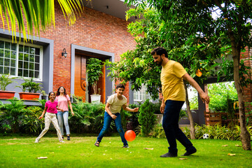 Indian parents and kids laugh and play ball game Piggy in the Middle in backyard garden