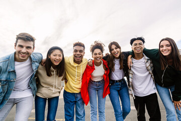 Young group of teenage friends smiling at camera hugging each other outdoors. Unity, friendship...