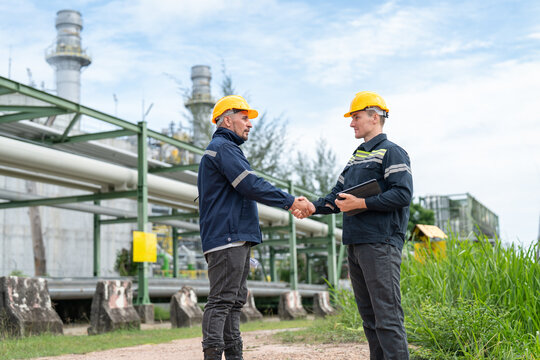 Two male petrochemical engineers shake hands after finishing work inspection and maintenance pipelines for oil and gas at petroleum refinery, power plant energy industry manufacturing.