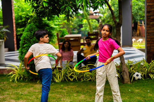 Smiling Indian parents watching kids play hula hoop in backyard garden on a sunny day