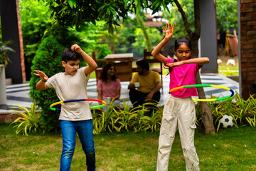 Smiling Indian parents watching kids play hula hoop in backyard garden on a sunny day