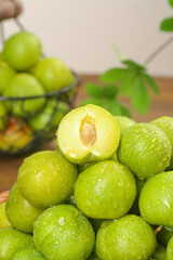 Fresh Sichuan Green Plums with Water Droplets and Exposed Pit on Wooden Table