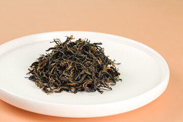 Organic black tea leaves with golden tips on white plate - loose leaf tea concept