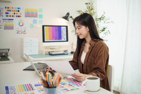 Young female graphic designer analyzing color charts, plans digital artwork in a bright workspace.