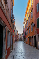 Fototapeta premium Empty colorful street in historic European town. Charming narrow street lined with colorful, aged buildings in a historic European town, captured in early morning light and silence.