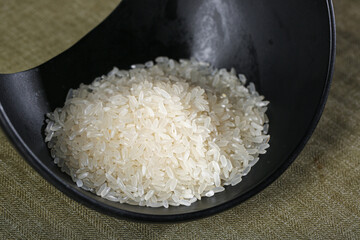 Fresh white rice grains in dark bowl - agricultural produce from cultivation ready for cooking