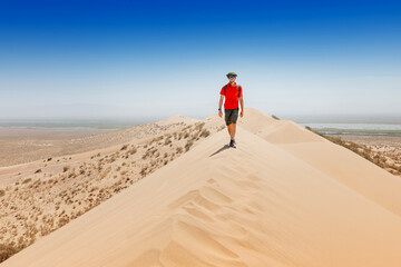 Tourist with backpack walking on sand dune in the desert during summer vacation, enjoying beautiful view
