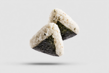 Two onigiri, traditional Japanese rice balls wrapped in seaweed, are floating elegantly against a white background. This unique presentation highlights their delicious texture and shape
