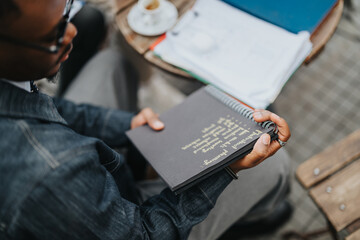 A person sitting outdoors reviewing handwritten notes in a notebook, suggesting focus and productivity. The setting suggests a business context or a casual workspace environment.
