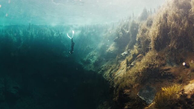 Freediver swims underwater in the crystal clear karst lake. Woman dives and glides underwater with fins in the blue lake. The lake named Goluboye Ozero, Samara, Russia