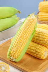 Fresh Sweet Yellow Corn on the Cob with Green Husks on Wooden Cutting Board