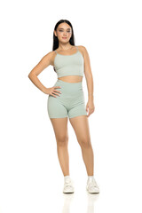 Fototapeta premium Studio shot of full length young woman with long black hair in mint green activewear and white sneakers, standing on white background.