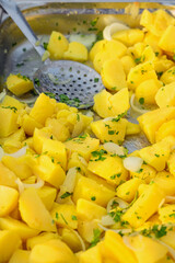 Freshly cooked yellow potatoes with chopped parsley and onion slices in a tray. Concept of boiled potatoes, vegetarian meal, and simple homemade food