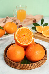 Fresh Orange Citrus Fruits in Wicker Basket with Juice and Sliced Segments on Kitchen Counter