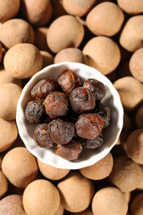 Dried Longan Fruit in Bowl with Fresh Longan Shells on Wooden Background