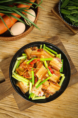 Wood-smoked bacon five-flower stir-fry dish with moss garlic in cast iron pan on wooden table