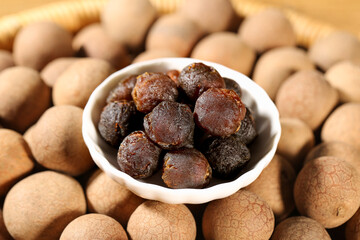 Dried longan fruits in white bowl surrounded by fresh longan shells - exotic Asian tropical ingredients