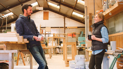 Male And Female Carpenter Working In Woodwork Workshop Talking On Coffee Break