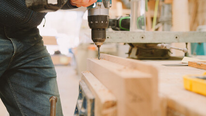 Close Up Of Carpenter At Workbench In Workshop Using Cordless Electric Drill