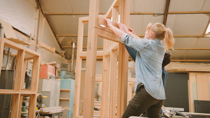 Male And Female Carpenters Working In Woodwork Workshop Making Window Frame Together