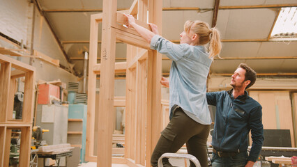 Male And Female Carpenters Working In Woodwork Workshop Making Window Frame Together
