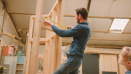 Male And Female Carpenters Working In Woodwork Workshop Making And Measuring Window Frame Together