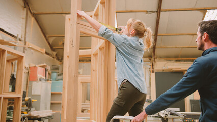 Male And Female Carpenters Working In Woodwork Workshop Making And Measuring Window Frame Together