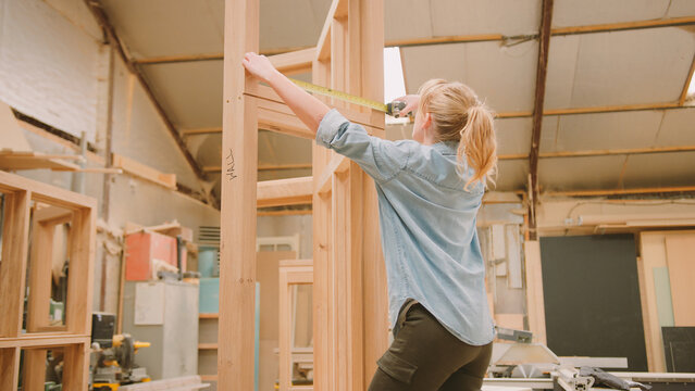 Female Carpenter Working In Woodwork Workshop Making And Measuring Window Frame