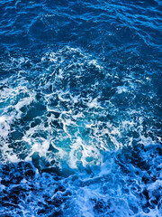 Fototapeta premium Water wave background. Turbulent ocean waves from above in blue tones. Aerial view. White wave splashing in the deep sea. Top view background photo of ocean sea water. Ocean surface. Navy blue.