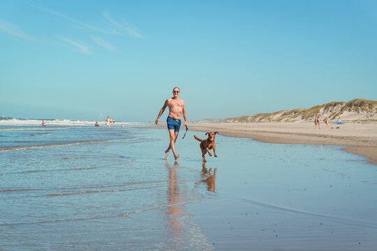 Man running with dog on beach during vacation in Denmark