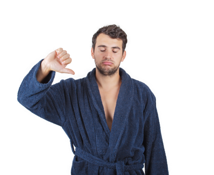 Displeased and sleepy young man hates waking up early morning. Fatigue male portrait, wearing bathrobe, shows thumb down negative gesture isolated on transparent background