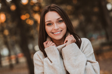 Beautiful young woman enjoying autumn outdoors in a cozy sweater, her radiant smile enhancing the charm of the fall season.