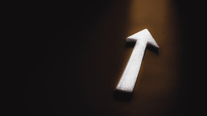A white arrow points exit towards the light on a dark background with copy space, symbolizing business direction, progress, success and strategy.