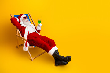 Santa Claus relaxing in a festive chair holding a holiday drink, enjoying a cheerful moment on a vibrant yellow background