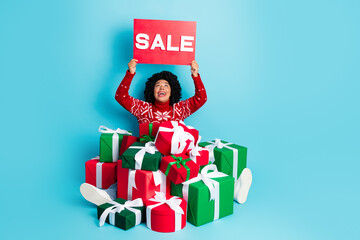 Festive woman in red Christmas sweater holding sale sign with colorful presents on a vibrant blue backdrop