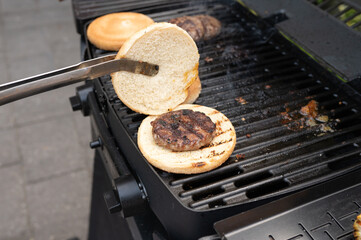 Grilling burgers: barbecue with open bun and beef patty on gas grill