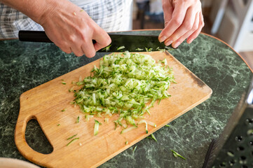 Adult caucasian male chopping cucumber on wooden cutting board in kitchen
