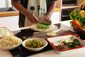 Man Cutting Long Beans with Fresh Vegetables on Kitchen Counter