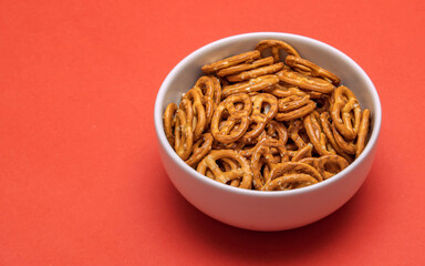 White bowl filled with crunchy salted pretzels on a red background. A simple snack arrangement highlighting the golden texture and savory appeal of this classic treat.
