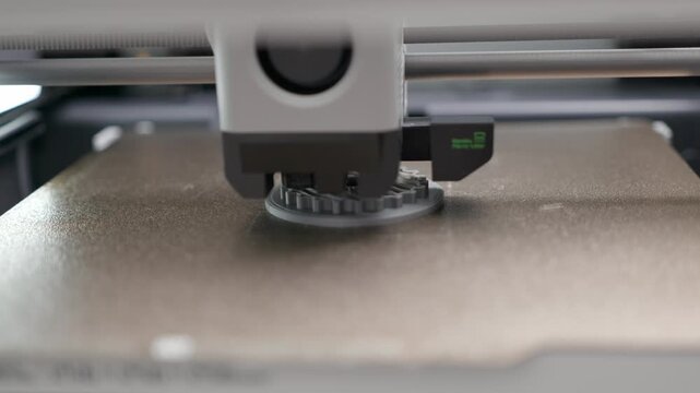 Extreme close-up of a 3D printer nozzle creating a prototype gear with gray filament, conveying additive manufacturing, rapid prototyping, and industrial innovation