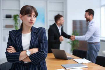 Woman feeling jealous of her successful colleague receiving congratulations in office, selective focus