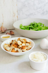 The process of cooking traditional Caesar salad with croutons and parmesan cheese on a gray table. The concept of traditional American cuisine. Horizontal orientation. Selective focus.