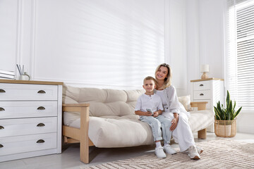 Woman and her son with air conditioner remote control on sofa at home